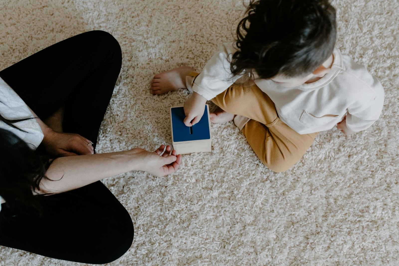 A mother and child engaging with a wooden toy on a cozy carpet indoors, promoting learning and bonding.